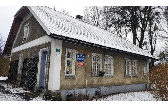 Domek Ogrodnika – Muzeum Zofii Kossak-Szatkowskiej w Górkach Wielkich od strony ulicy/wejścia, niewielki zabytkowy budynek z jasną elewacją, spadzistym dachem pokrytym śniegiem oraz oknami zabezpieczonymi kratami, listopad 2025.