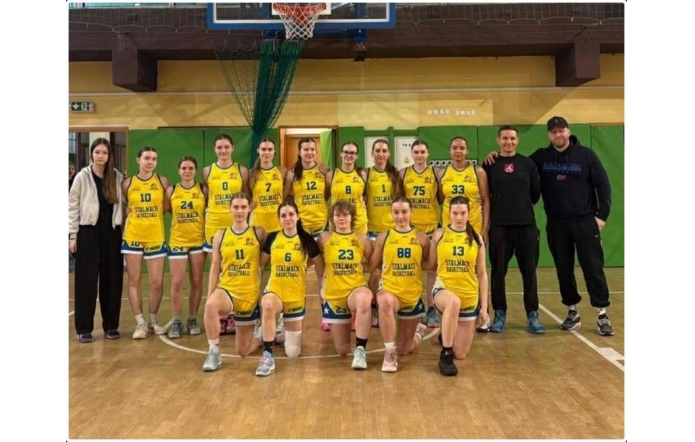 Grupa zawodniczek w żółtych strojach koszykarskich oraz trener na sali gimnastycznej pod koszem do gry.