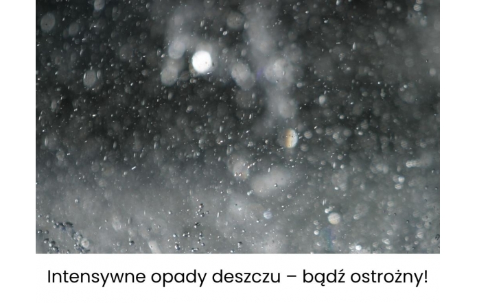 Rozmyte krople deszczu spadające w ciemności tworzą efekt mgiełki i refleksów świetlnych. U dołu białe tło z czarnym napisem: „Intensywne opady deszczu – bądź ostrożny!”.