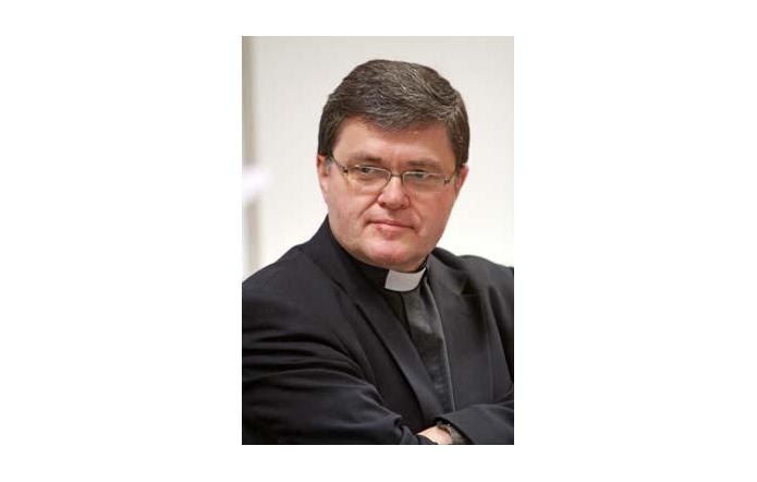 Ks. prof. Józef Budniak – duchowny katolicki i wykładowca akademicki, ubrany w klasyczną czarną sutannę z koloratką i marynarkę, z poważnym i zamyślonym spojrzeniem. Portret wykonany na jasnym tle.