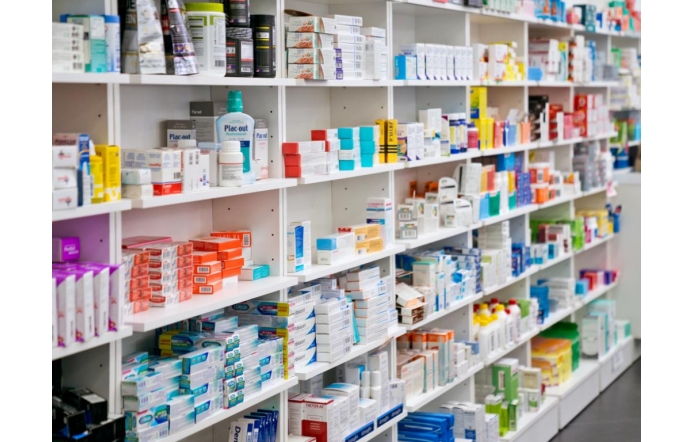 Kolorowe opakowania leków i suplementów ułożone na białych półkach w aptece tworzą uporządkowany, przejrzysty regał z szerokim wyborem produktów farmaceutycznych i higienicznych.
