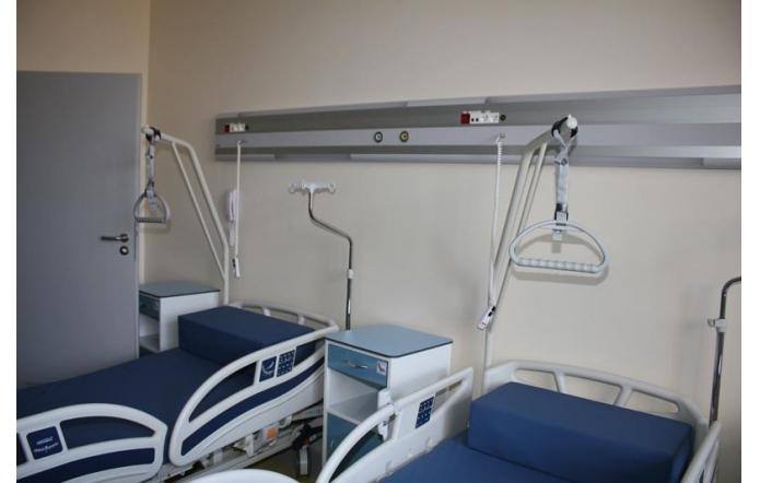 W pomieszczeniu znajdują się dwa łóżka szpitalne z niebieskimi materacami. Nad nimi zamontowane są uchwyty i wysięgniki do podciągania się oraz panel z instalacjami medycznymi. Między łóżkami stoi mała szafka.